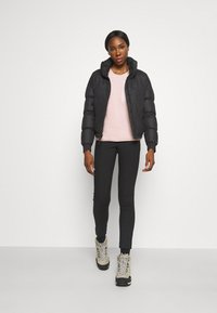 Svart pufferjacka med huva, ljusrosa fleece-tröja, svarta leggings och grå vandringskängor med svarta sulor och silverfärgade snören.