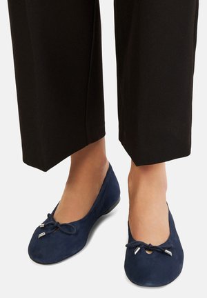 Bailarinas de ante azul marino con punta redonda, que cuentan con un pequeño lazo y acentos metálicos, combinadas con pantalones de pierna ancha negros.