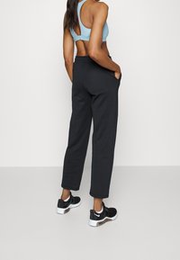 Czarne spodnie dresowe z bocznymi kieszeniami, o luźnym kroju i elastycznym pasie, zestawione z czarnymi trampkami i jasnoniebieskim stanikiem sportowym.