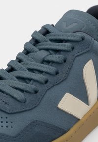 Sneaker blu in suede con lacci piatti, dettagli perforati e accento del logo crema. Suola in gomma con finitura testurizzata.
