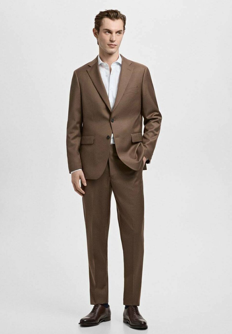 Costume marron avec revers crantés, fermeture à un bouton et deux poches avant. Associé à une chemise bleu clair et des chaussures marron.