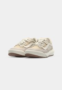 Lys beige sneakers med en teksturert overdel, hvite detaljer og rund tå. Har snøring og såle av gummi med mønstrede riller.