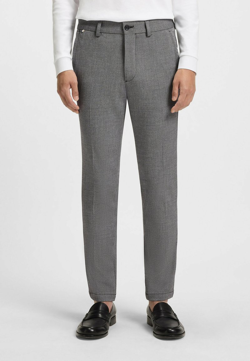 Szare, teksturowane spodnie o prostym kroju, z przednimi kieszeniami, zamkiem błyskawicznym i zapięciem na guzik, oraz mankietami. Noszone z czarnymi mokasynami.