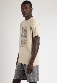 Camiseta de algodón beige con diseño gráfico de texto, combinada con pantalones cortos grises que presentan un sutil estampado de animales. Ajuste suave y casual.