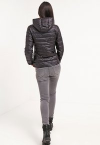 Doudoune noire à capuche, design matelassé vertical et texture lisse. Associée à un pantalon gris ajusté et des bottines noires.