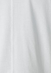Cămașă albă cu mânecă scurtă, cu o textură netedă și ușoară. Prezintă o cusătură subtilă pe mijloc. Design curat și minimalist.