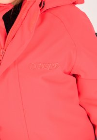 Skallig korallfärgad vattentät jacka med dragkedja, utrustad med "ZIGZAG"-logotyp i diskret broderi på bröstet. Slät, strukturerad tyg.