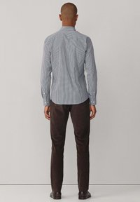 Camisa de cuadros azul y blanca con mangas largas, cuello abotonado y dobladillo curvo, combinada con pantalones marrón oscuro.