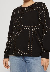 Svart långärmad sweatshirt med ett beige prickmönster. Tillverkad av mjukt material, med rund halsringning och ribbade ärmslut.