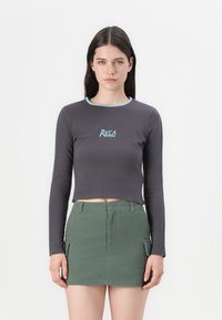 Dlhý rukáv, tmavosivý crop top so svetlomodrým výstrihom a logom RVCA. V kombinácii so zelenou mini sukňou s cargo vreckami.