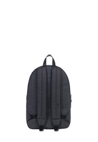 Mochila de tela gris con forma redondeada, correas ajustables acolchadas y bolsillo frontal con cremallera. Textura suave, diseño minimalista, sin patrones visibles.