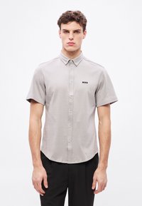 Szara koszula z krótkim rękawem i kołnierzem zapinanym na guziki, wykonana z fakturowanej tkaniny, z czarnym logo "BOSS" na lewej piersi.