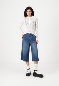 Top alb cu dantelă, cu mâneci lungi și model floral, asociat cu pantaloni culottes din denim albastru, cu picioare ample, și pantofi cu platformă negri, cu brâu la gleznă.