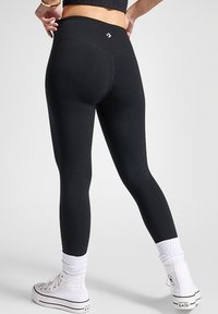Černé legíny s vysokým páskem, přiléhavým střihem a hladkou texturou. Kombinované s bílými vysokými teniskami a žebrovanými kotníkovými ponožkami.