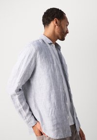 Striped button-up shirt in light blue and white, featuring a relaxed fit, collar, and long sleeves. Made of textured fabric with a casual design.