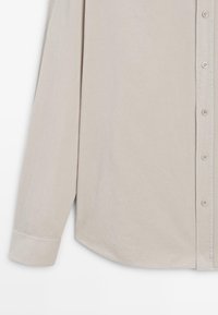 Camicia beige a maniche lunghe con chiusura a bottoni, texture liscia, orlo curvo e maniche con polsini, con bottoni coordinati lungo la patta.