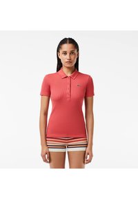 Polo rojo de canalé con cuello clásico y tapeta de tres botones, que presenta un pequeño logo verde en el lado izquierdo del pecho.