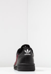 Czarne skórzane trampki z czerwonymi akcentami, z fakturowanym wykończeniem, wyściełanym kołnierzem i białym logo Adidas z tyłu.