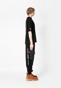 Camiseta negra de gran tamaño con un gráfico en la parte posterior, combinada con joggers negros con un bolsillo lateral y botas de senderismo marrones con suela resistente.