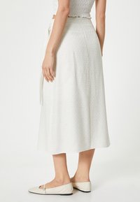Witte midi-rok met een geweven patroon, vastgebonden in de taille. Gecombineerd met lichtgekleurde platte schoenen.