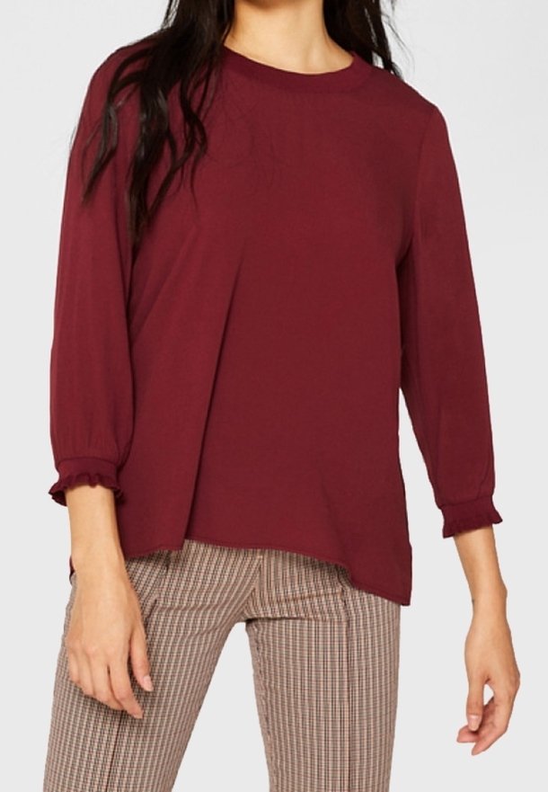 Bordowa bluzka z rękawami w kształcie puff, sięgającymi do łokci i falbaniastymi mankietami, z okrągłym dekoltem, w połączeniu z brązowymi spodniami w kratę.