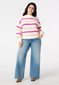 Pull blanc avec des rayures horizontales roses et orange, manches larges, associé à un jean évasé bleu clair et des bottines marron.