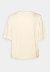 Chemise à manches courtes de couleur crème pâle, en matière douce, avec un col arrondi et une coupe décontractée. Design simple, sans motifs ni accents.