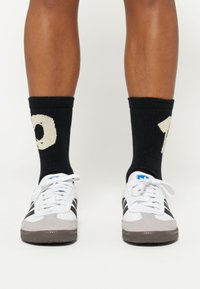 Hvide og grå sneakers med sorte striber, parret med sorte sokker med et cremefarvet nummer 10 strikket design.
