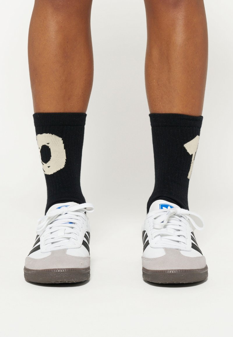 Hvide og grå sneakers med sorte striber, parret med sorte sokker med et cremefarvet nummer 10 strikket design.