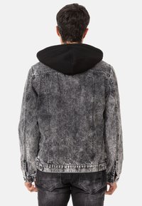 Jeansjack met een vervaagde grijze afwerking, zwarte stoffen voering in de capuchon, knoopjes bij de manchetten en stikseldetails. De achteraanzicht toont een relaxte pasvorm.