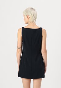 Robe noire sans manches avec un décolleté bateau et une silhouette ajustée. Le tissu a une texture lisse et présente une couture au dos au centre.