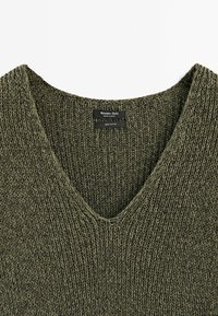 Pull vert en maille à col en V avec une étiquette indiquant la marque Massimo Dutti, fabriqué en Espagne, et information sur le matériau 100 % coton.