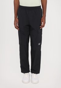 Pantalons cargo noirs avec une taille élastique, deux poches latérales et un petit logo EA7 sur la jambe gauche. Fabriqués en tissu léger.