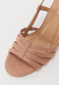 Riemchen-High-Heel-Sandale aus zartem rosa Wildleder. Verfügt über mehrere horizontale Riemen und eine glatte, abgerundete Zehenpartie mit einer hellbraunen Innensohle.