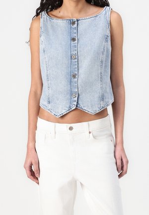 Lichtblauw denimvest zonder mouwen met vijf knopen aan de voorkant, gecombineerd met hoge taille witte broek gedragen door een persoon.