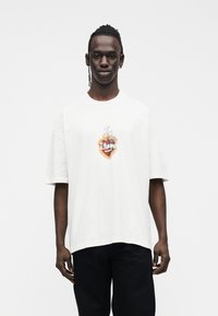 White cotton oversized t-shirt featuring a colorful heart graphic with "ALLSAINTS" text, short sleeves, and a relaxed fit.