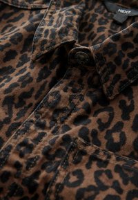Chemise à imprimé léopard brun avec des taches noires, dotée d'un col, d'une fermeture à boutons et de détails cousus. Fabriquée en tissu texturé.