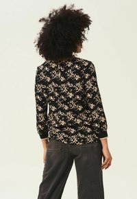 Svart blus med beige blommönster, långa ärmar och rund halsringning. Har en knappstängning bak och något lös passform.