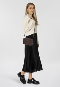 Suéter de punto beige, falda plisada negra y zapatos de plataforma negros brillantes. Bolso cruzado marrón con diseño texturizado y correa de cadena.