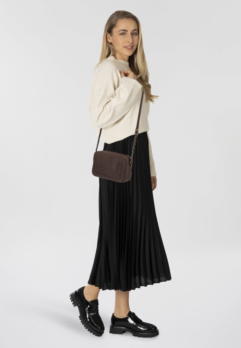 Suéter de punto beige, falda plisada negra y zapatos de plataforma negros brillantes. Bolso cruzado marrón con diseño texturizado y correa de cadena.