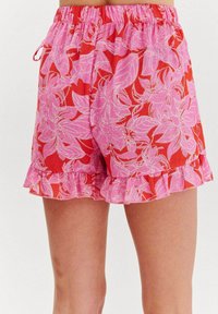Červené šortky s ružovým kvetinovým vzorom, s elastickým pásom a volánovým lemom. Vyrobené z ľahkej tkaniny s hladkou textúrou.