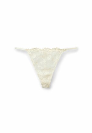 Lace thong in off-white, featuring scalloped edges and thin straps. Floral pattern is visible on the lace material.
