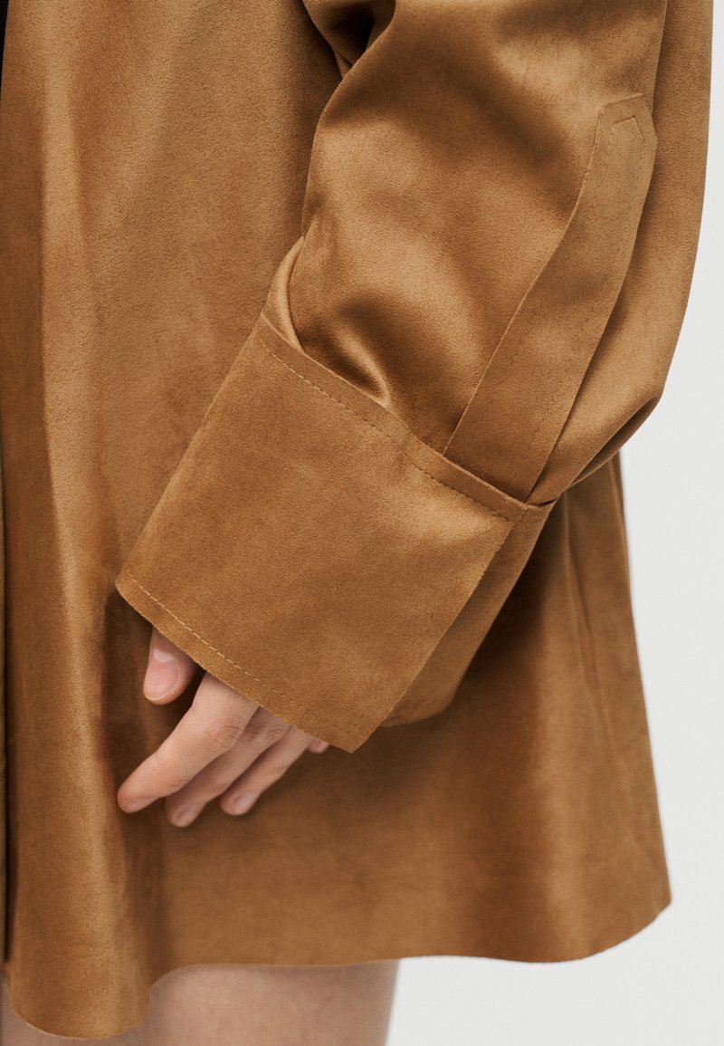 Braunes Hemd aus Kunstwildleder mit breitem Manschettenabschluss und weicher Textur, mit glatter, leicht glänzender Oberfläche und sauberem Saum.