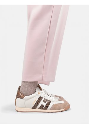 Persoon draagt lichtroze broek, taupe sokken en witte sneakers met bruine gestructureerde accenten en beige suède details, gezien van opzij.