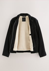 Veste en velours côtelé noir avec devant ouvert révélant une doublure polaire crème et une étiquette à l'intérieur du col.