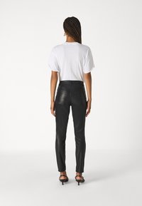 Svarta läderbyxor med slim fit och hög midja, med en slät yta och minimalistisk design, tillsammans med en vit t-shirt.