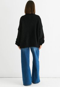 Black knitted sweater with a relaxed fit, featuring drop shoulders and ribbed hem, paired with wide-leg blue denim jeans.