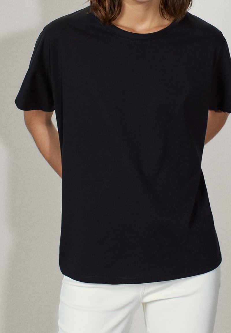 Czarny t-shirt z krótkim rękawem, uszyty z miękkiej tkaniny, z klasycznym okrągłym dekoltem i luźnym krojem. W zestawie z białymi spodniami.