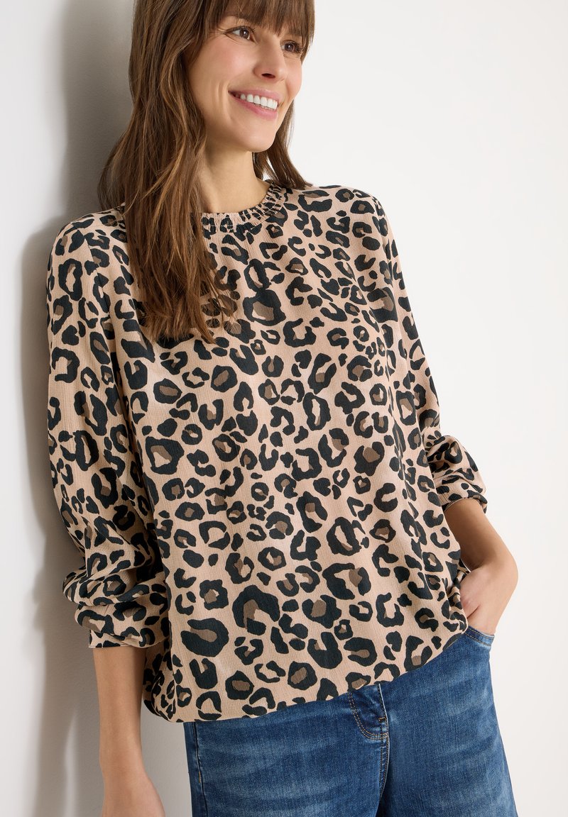 Leopardmuster-Pullover in Beige mit schwarzen Flecken; verfügt über einen Rundhalsausschnitt und locker sitzende Ärmel, kombiniert mit blauen Jeans aus Denim.