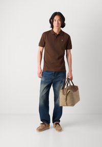 Braunes Polohemd, Jeans im Denim-Stil und eine beigefarbene Tasche mit braunen Akzenten. Legere Schuhe runden das Outfit ab. Einfaches, funktionales Design.